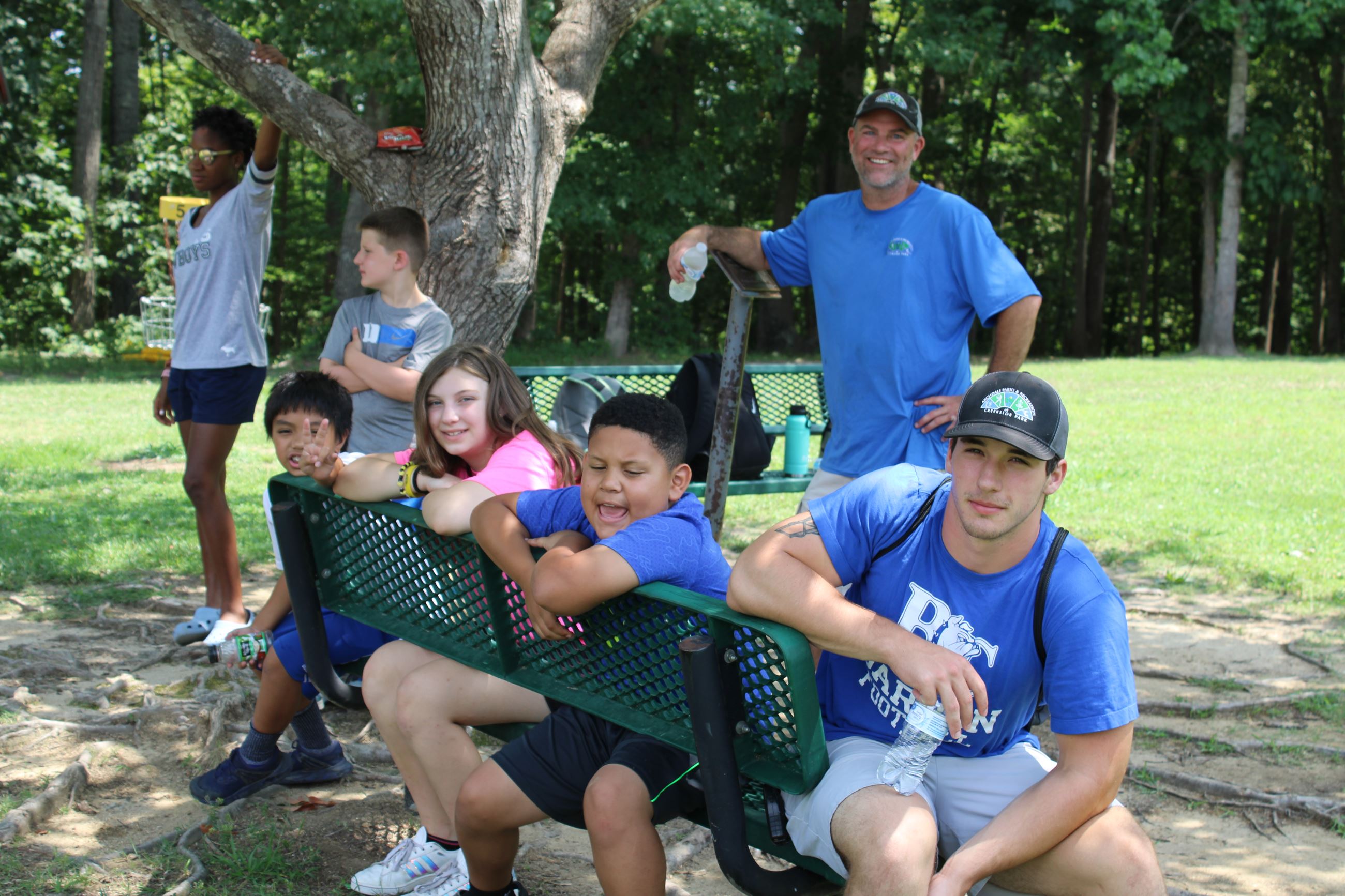 Counselor in blue shirt, Athletic Director, and 3 kids in the afterschool program chill on a bench